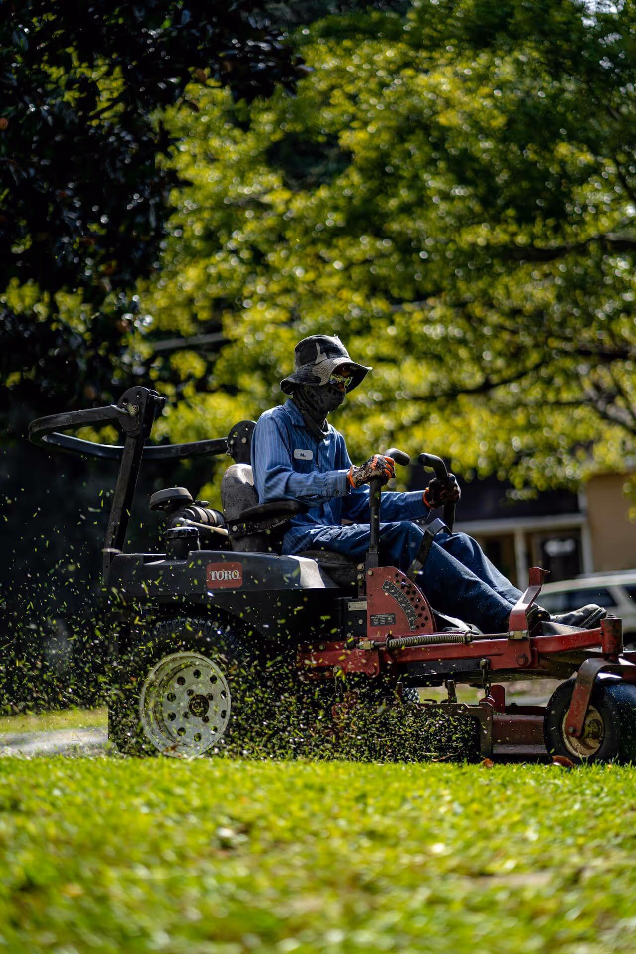 Person wearing sun protection clothing operating a Toro riding lawn mower cutting grass on a sunny day.